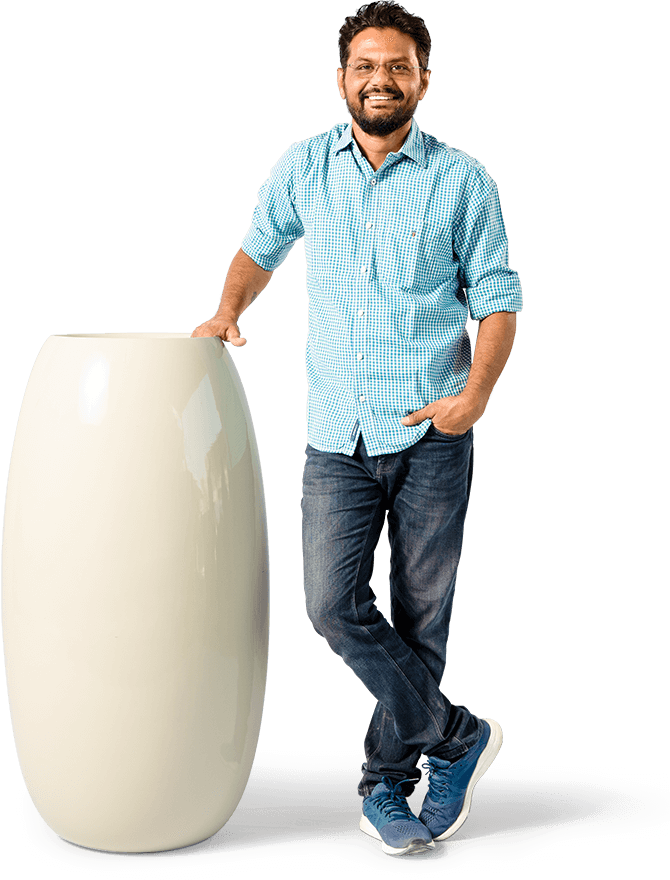 a man with smiling face standing besides a large planter in blue colored shirt & jeans